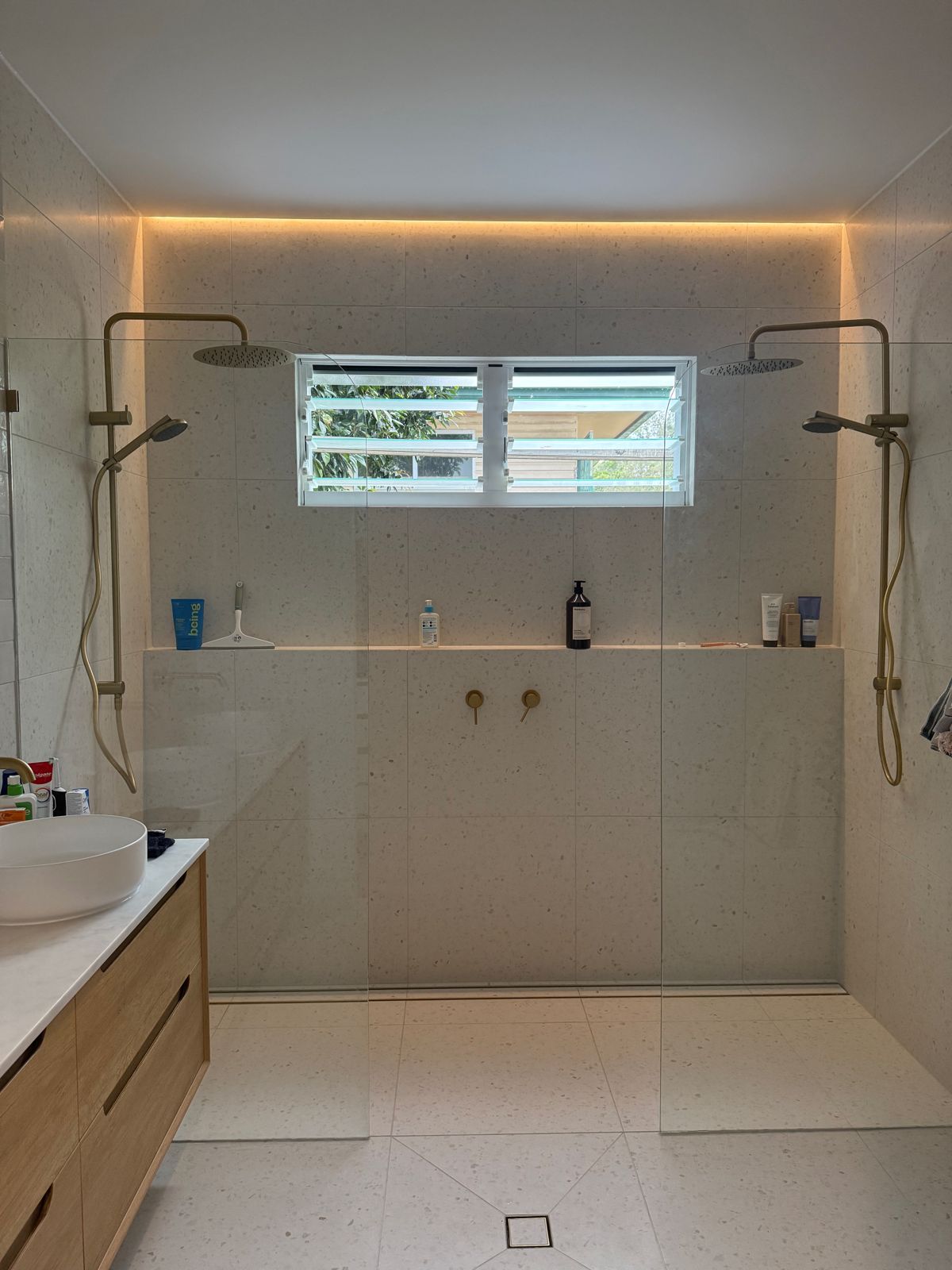 The finished bathroom: double rain showers, brass tapware, a strip light over the niche and a timber vanity