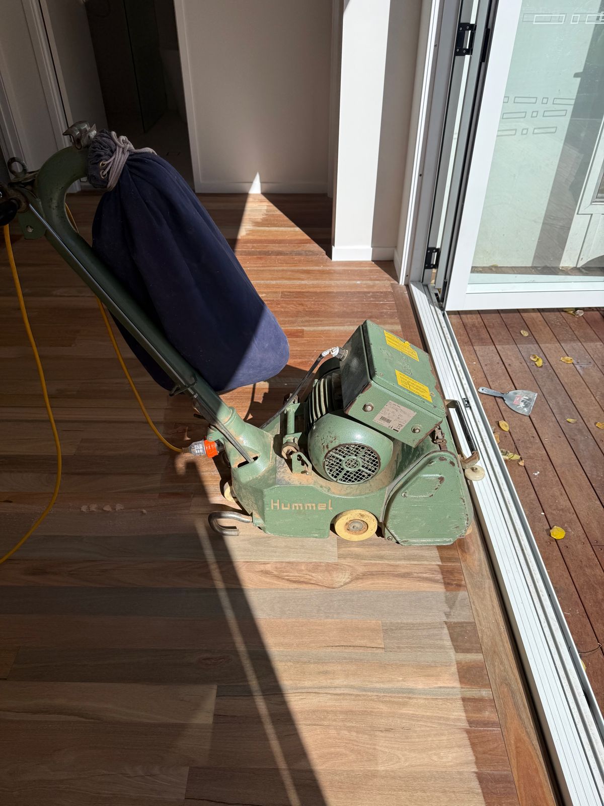 A floor sander on hardwood boards beside open sliding doors