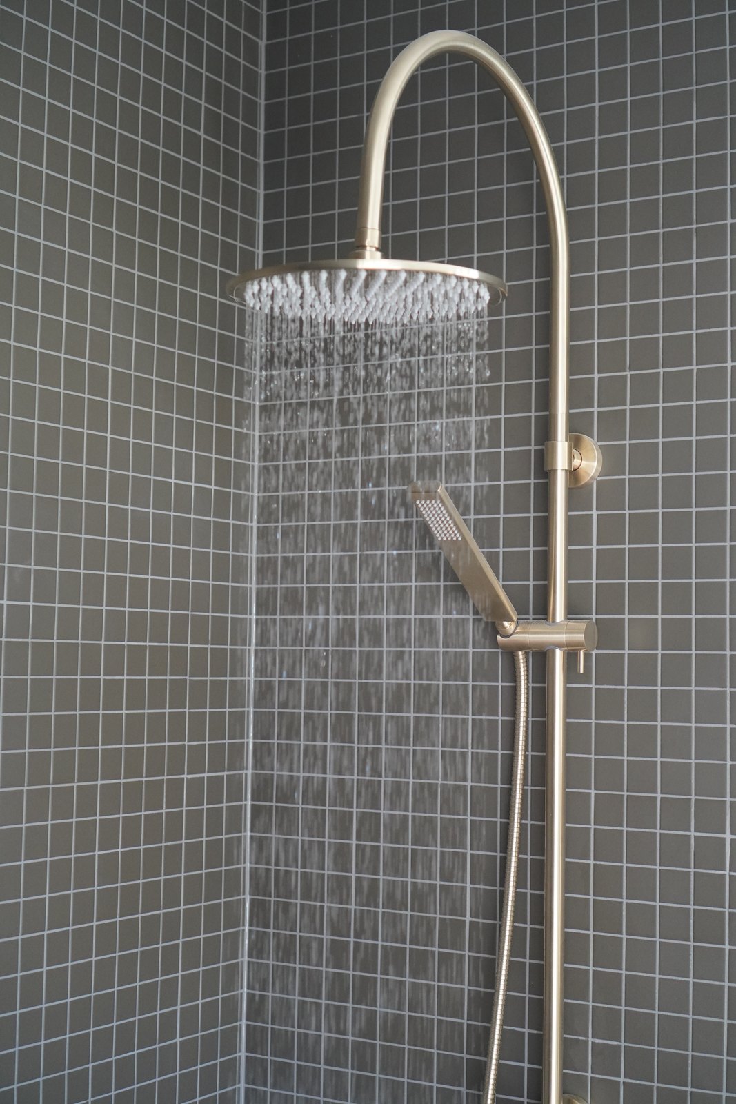 A brushed brass rain shower running against dark square tiles in a finished Outhaus bathroom