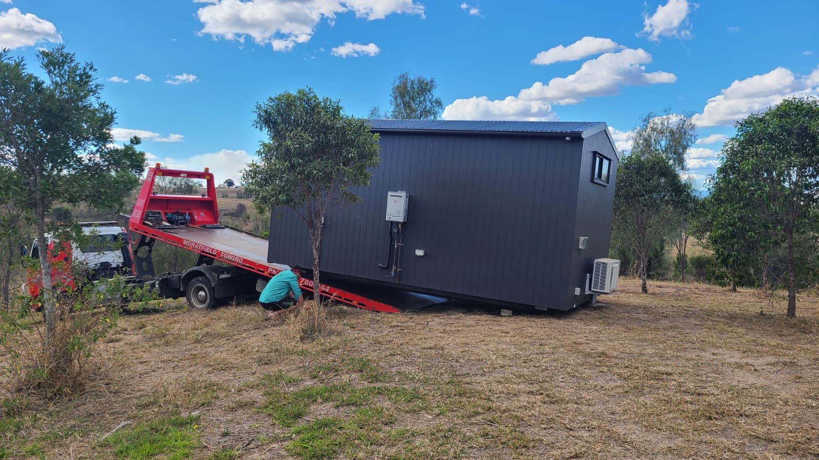 A dark second home arriving on a tilt tray truck at a rural block