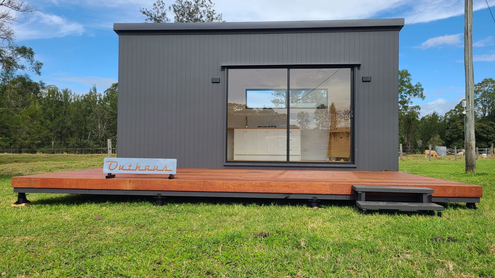 A finished dark-clad second home with a timber deck on a green lawn