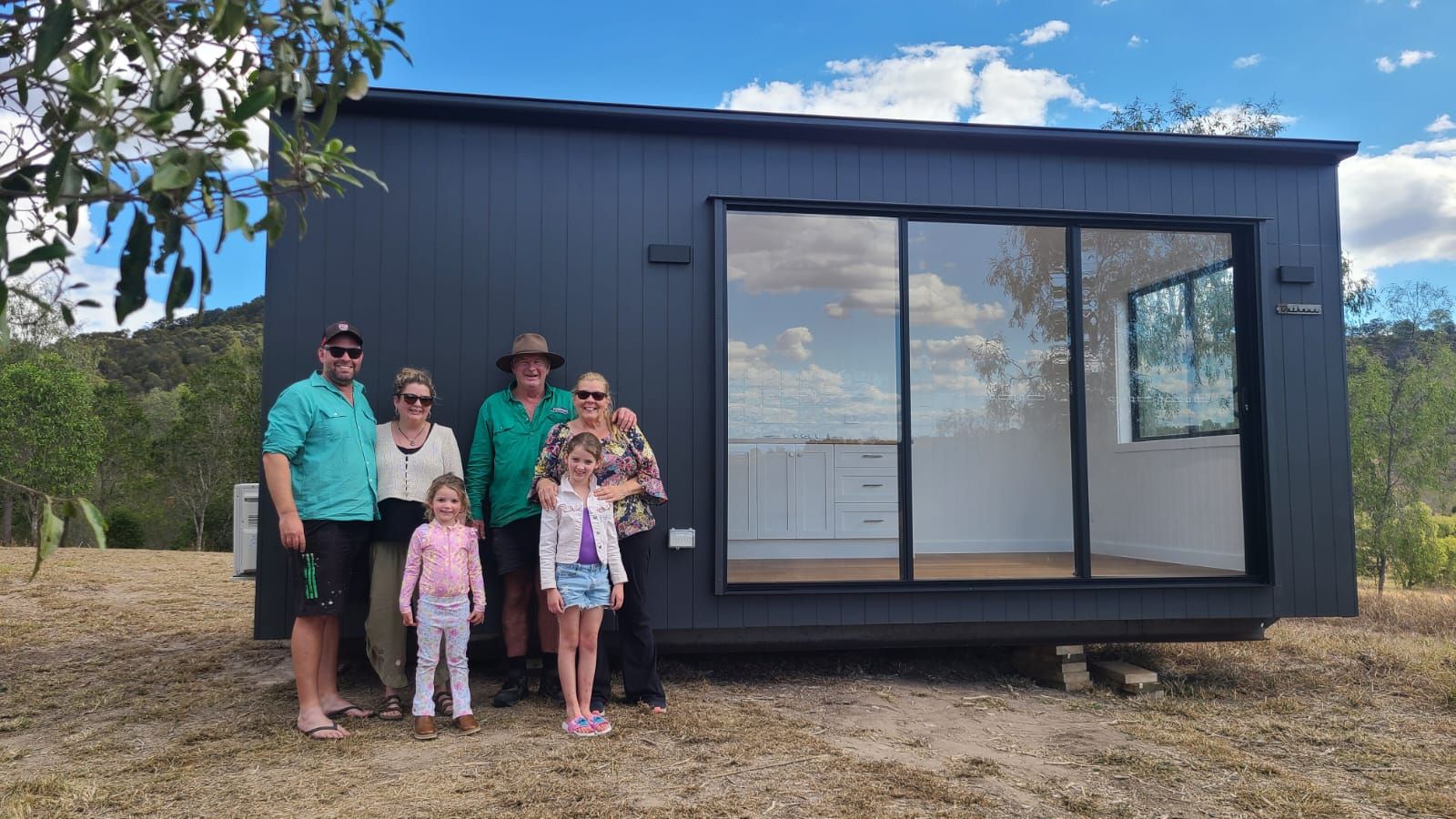 A family of six standing in front of their new dark-clad second home on handover day