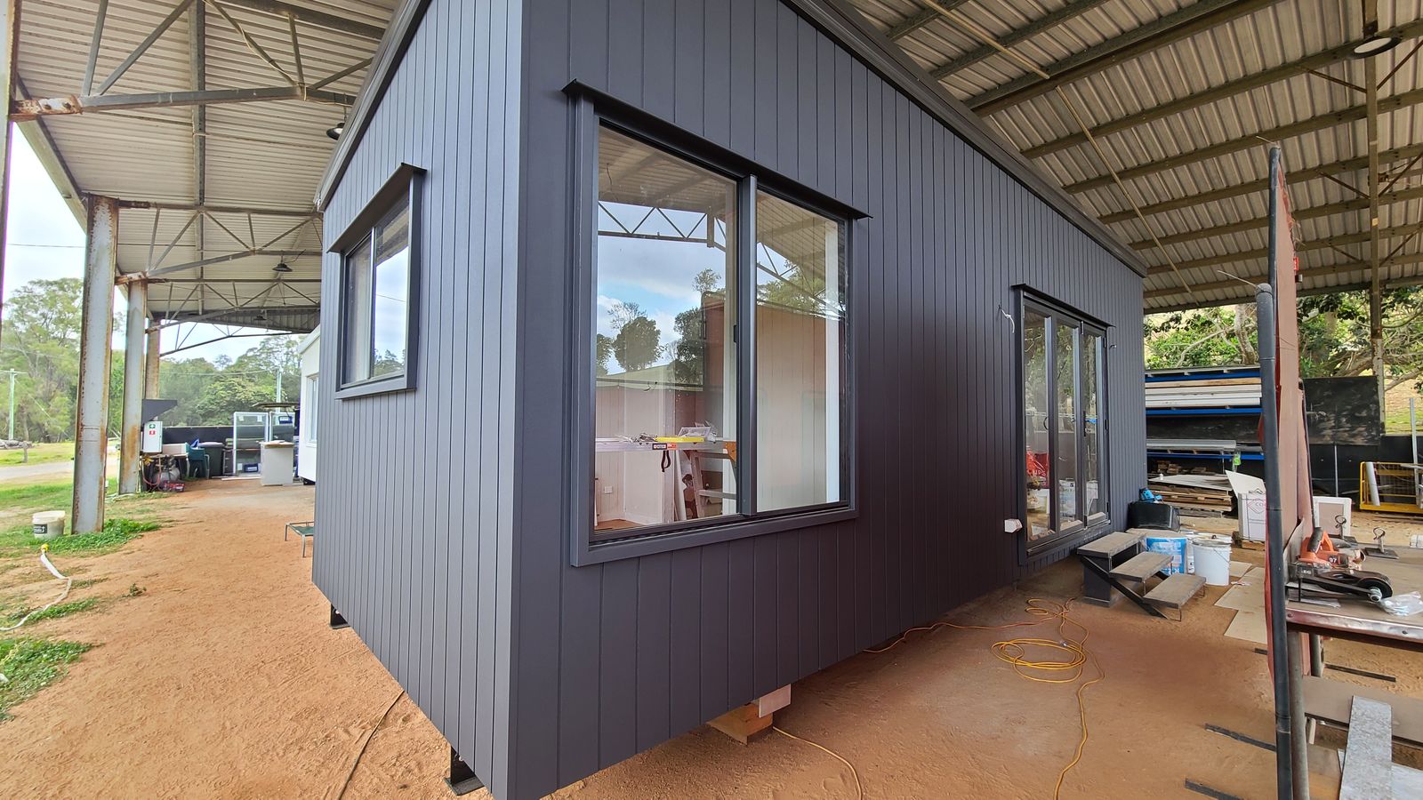 A finished dark-clad 8.4 metre modular home on stands in the factory, ready to be trucked to site