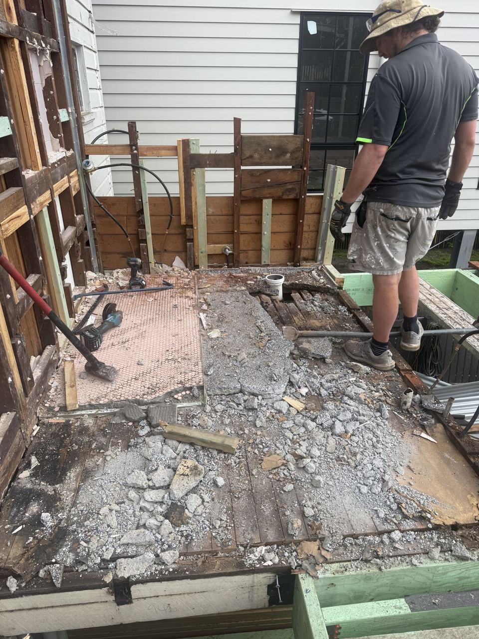 A builder standing in a gutted bathroom, old tiles and floor broken out down to the joists