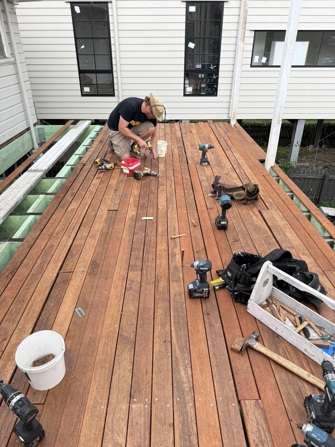 A carpenter kneeling to fix hardwood decking boards on the new deck, tools spread around him