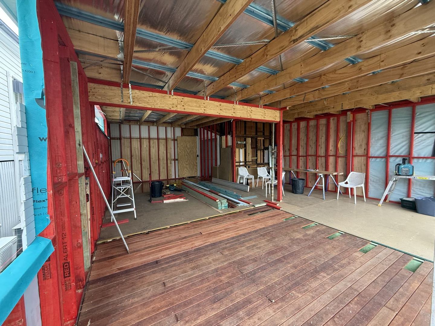 Inside a framed timber extension on an old Queenslander, red LVL wall frames, open roof framing and a new hardwood floor