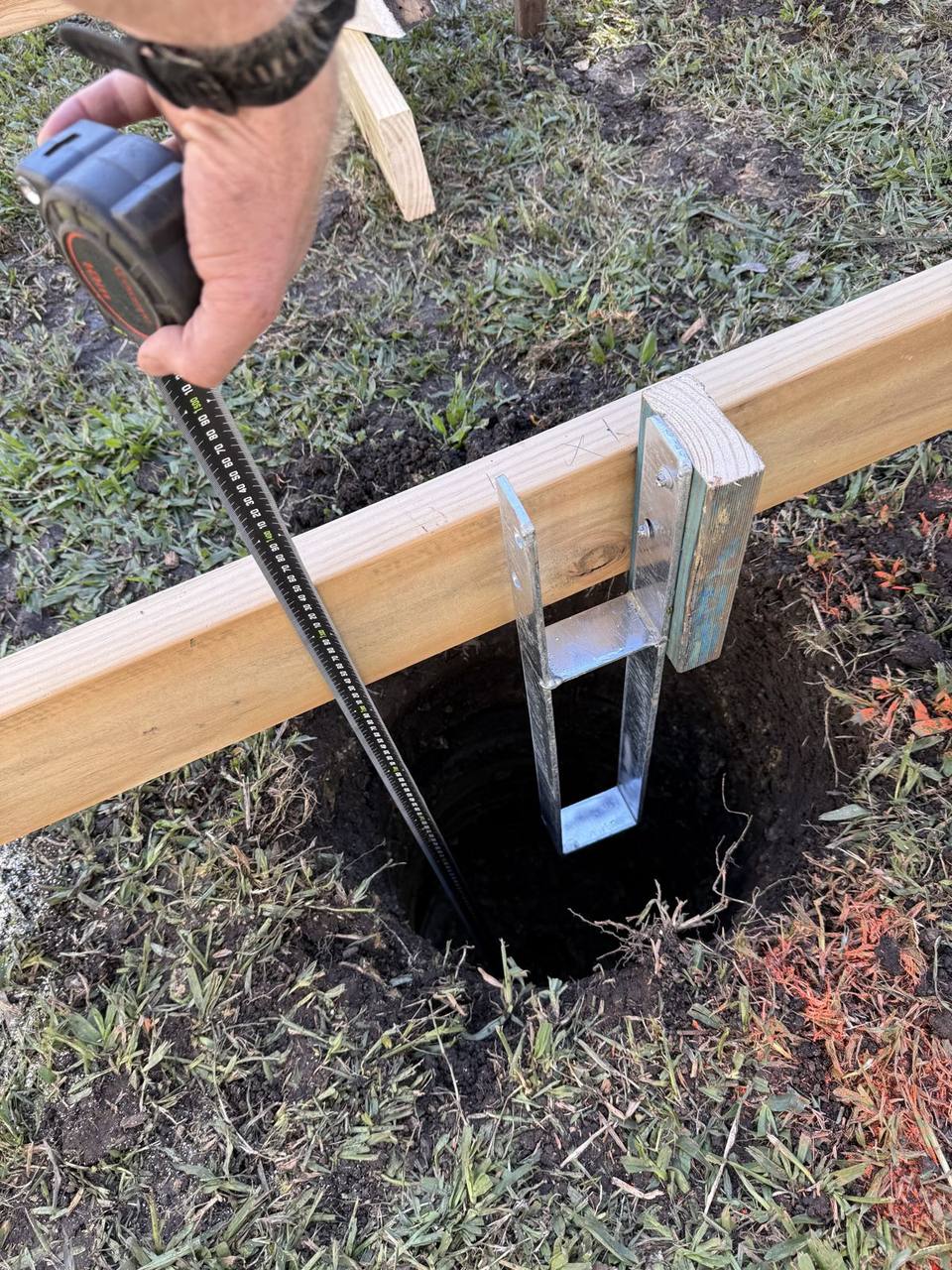 A tape measure checking the height of a galvanised pier bracket set in a footing hole against a timber string line