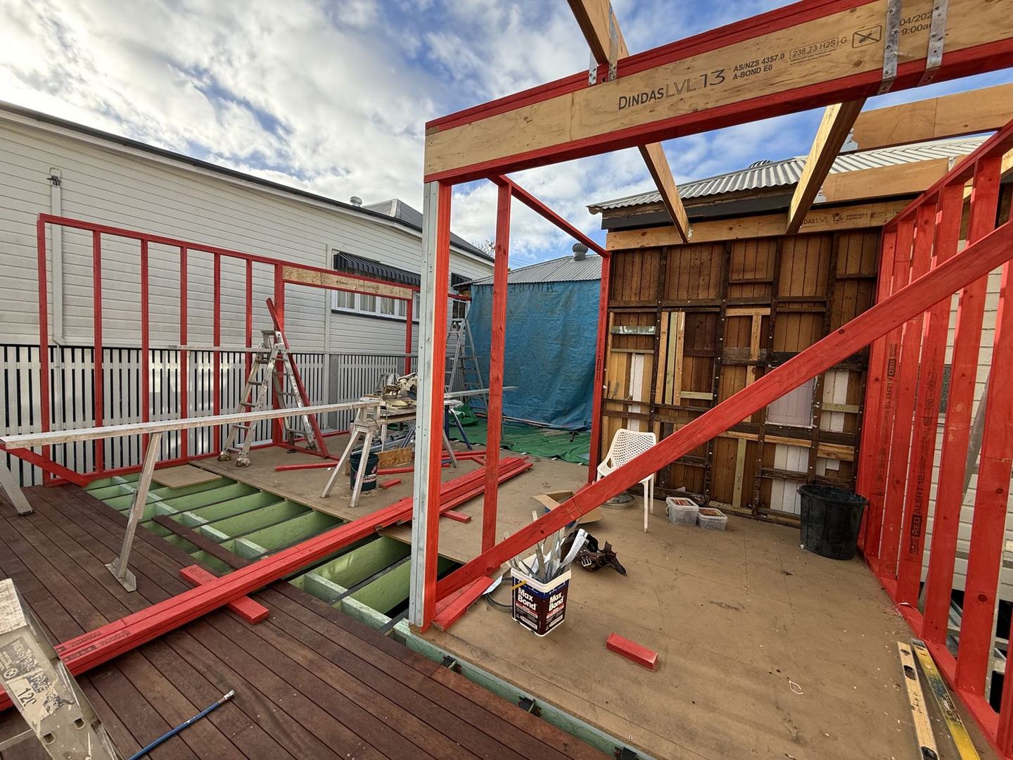 Red LVL wall frames standing on the new floor platform, braced against the old weatherboard wall