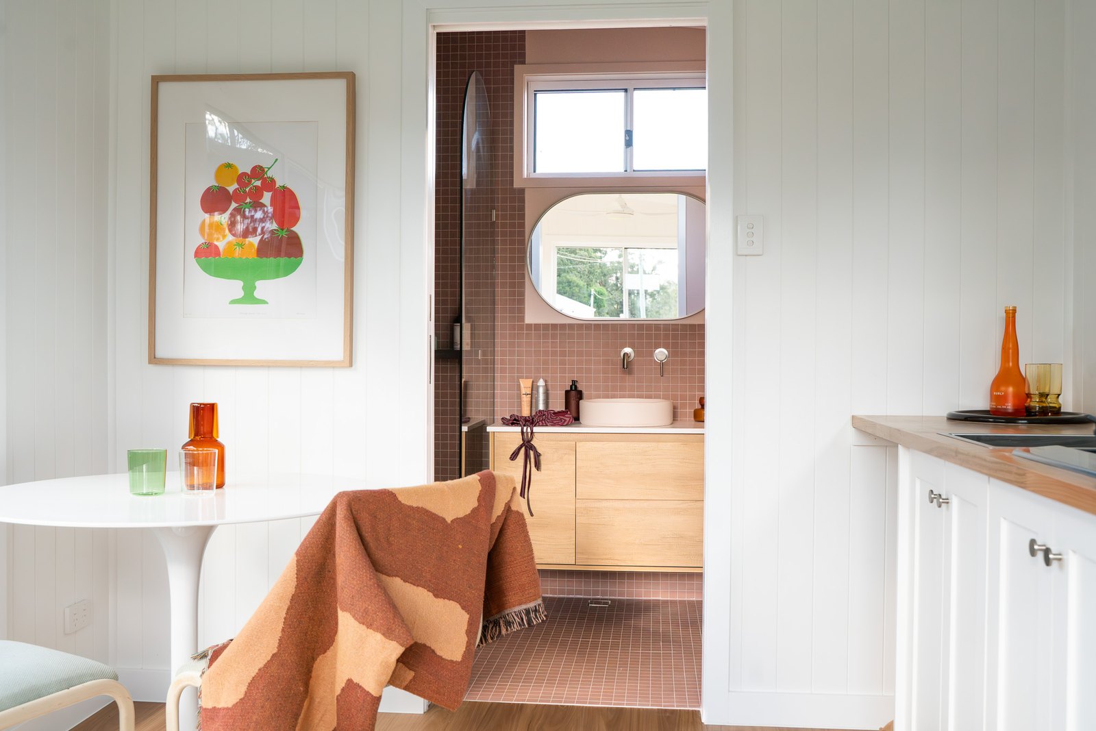 Inside a finished white Outhaus 6.0 x 3.0, a round white table, the kitchen bench and the pink-tiled bathroom through the door