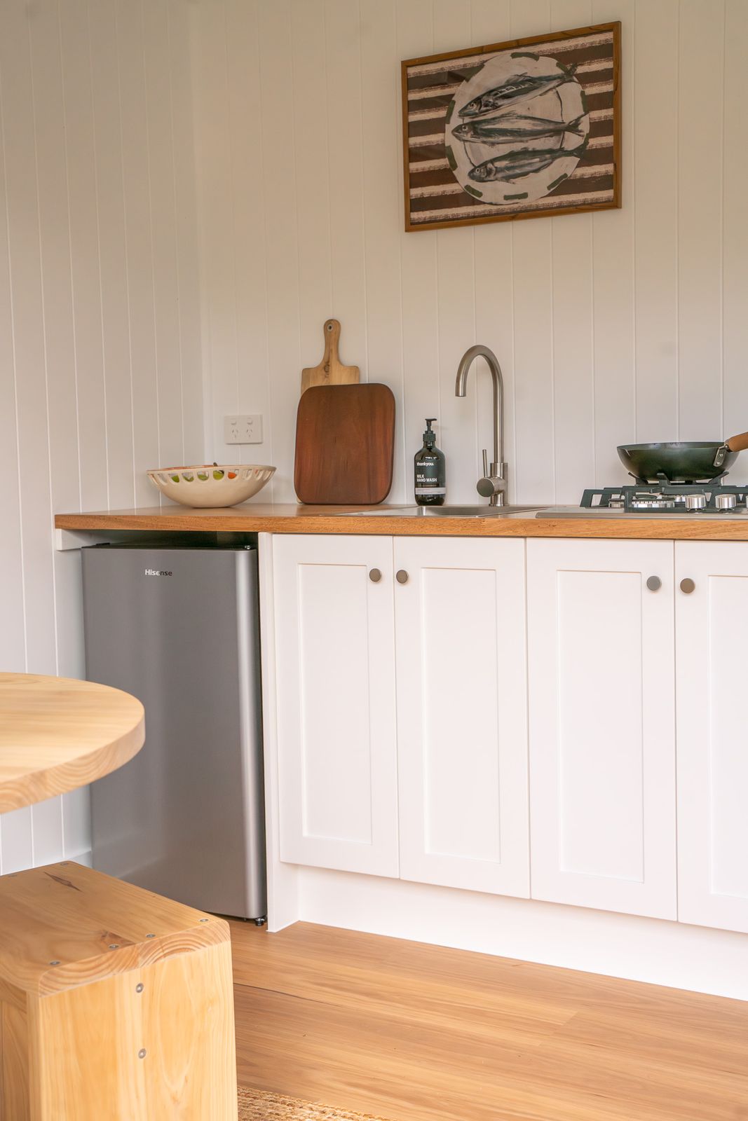 Inside a finished second home, a white shaker kitchen with a timber benchtop, gas cooktop and bar fridge