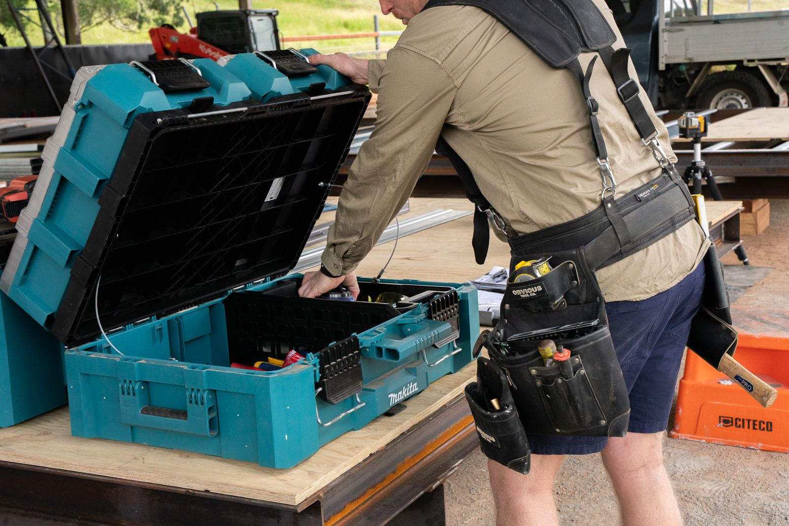 A carpenter in a tool belt opening a stack of tool cases on the workbench